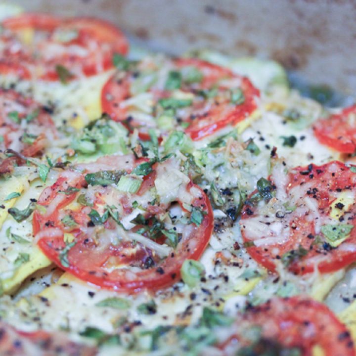 Cooked dish of layered slices of tomatoes, zucchini, yellow squash, and cheese with herbs and spices