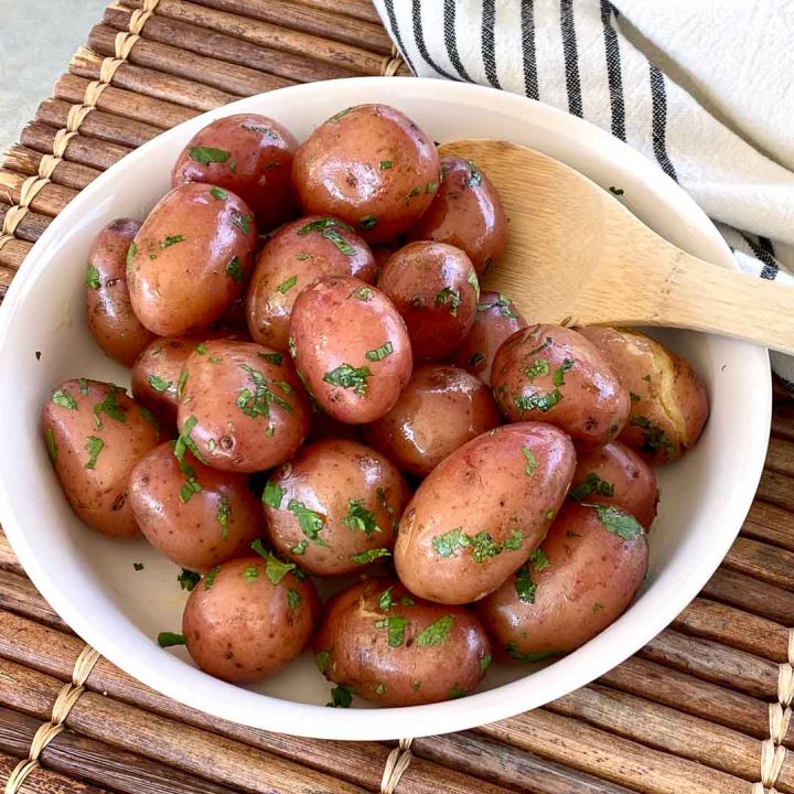 Boiled red potatoes buttered and garnished with parsley in a white bowl with a wooden spoon