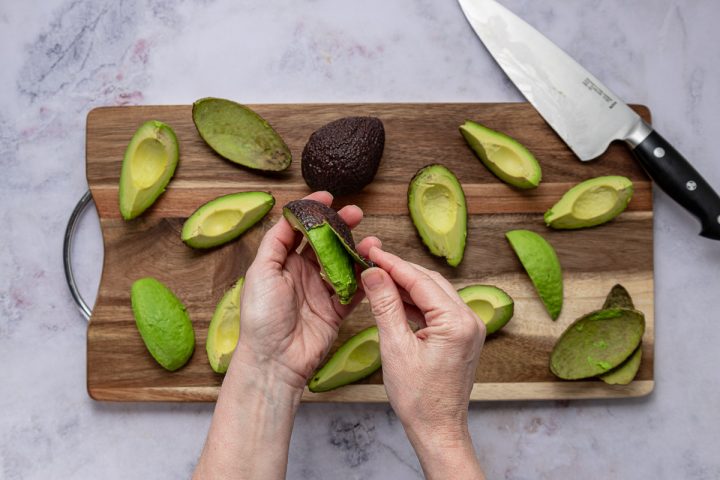 Several quartered and pitted avocados on a cutting board