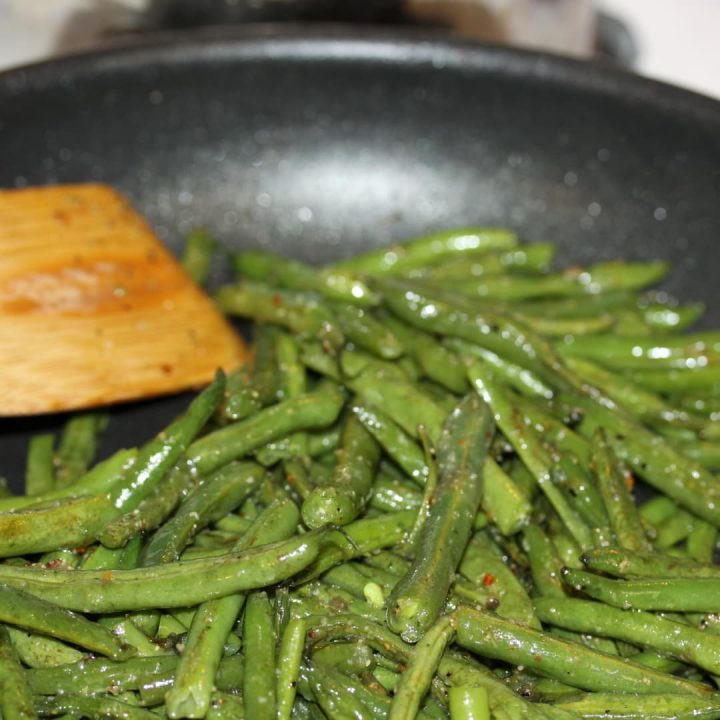 Sautéed seasoned green beans in a black frypan