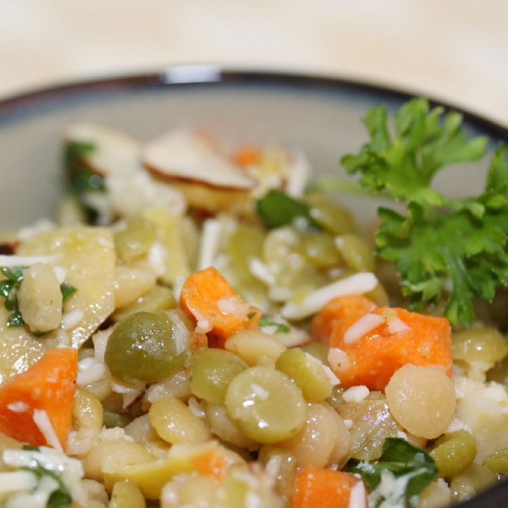 Lentils, carrots, artichokes, and almonds in a bowl topped with dressing and shredded parmesan cheese, garnished with parsley