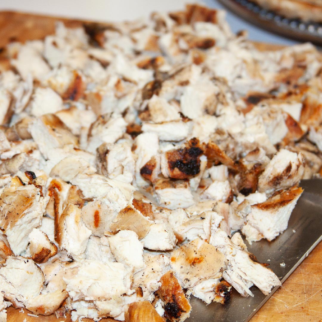 Chopped grilled chicken on a cutting board with a knife