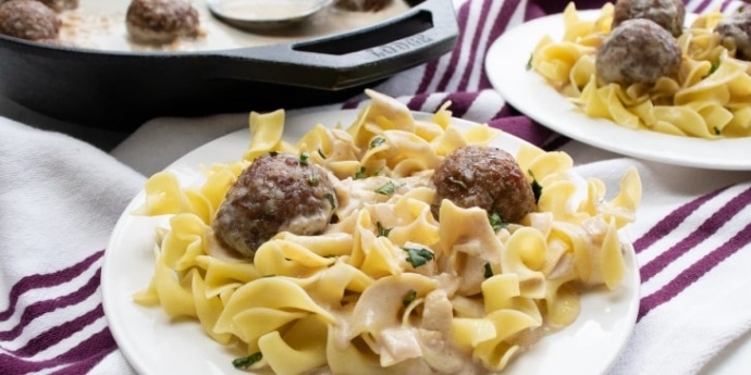 Meatballs in a cream sauce over egg noodles and a cast iron skillet in the background