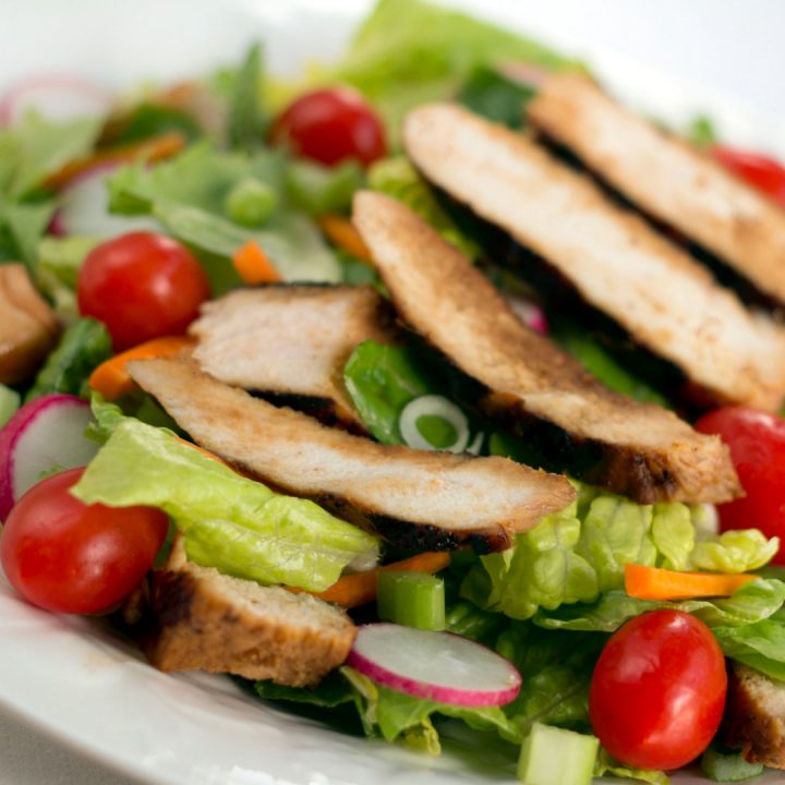Salad of romaine lettuce pieces, grape tomatoes, and carrots topped with sliced grilled chicken