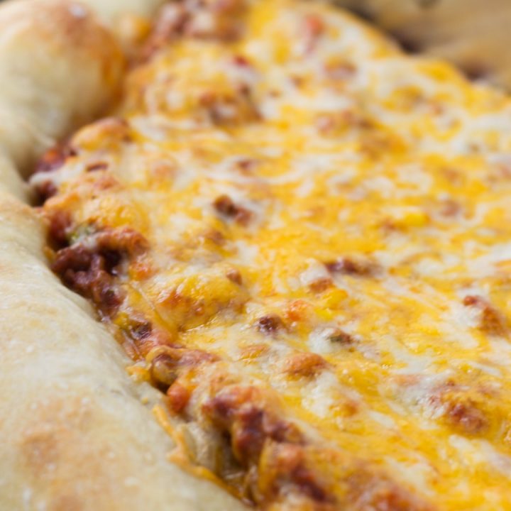 Side view of a whole pizza with sloppy joe sauce covered with colby-jack cheese on a thick crust