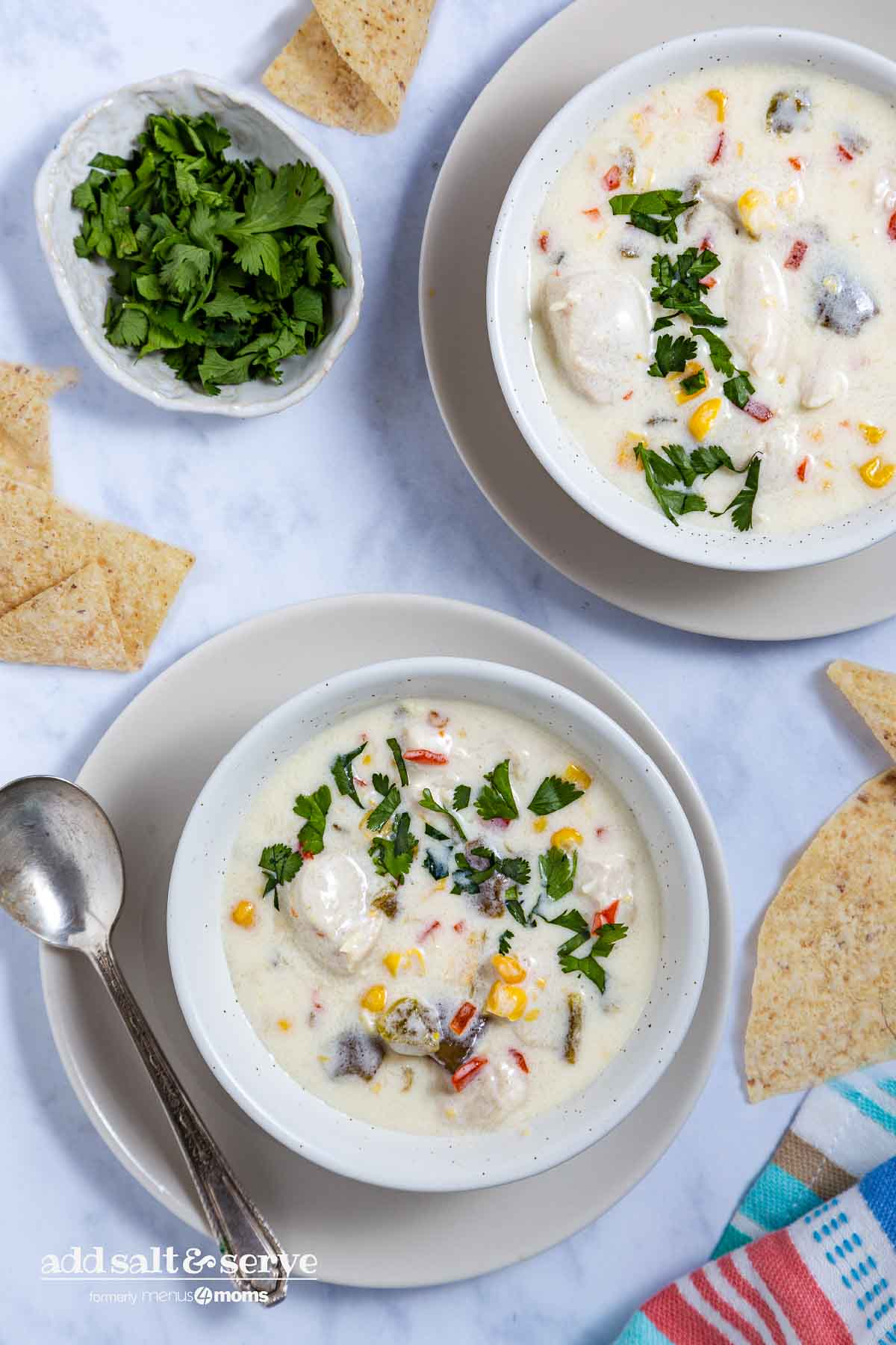 Two bowls of Southwest Chicken Corn Chowder on saucers with cilantro and tortilla chips to the side.