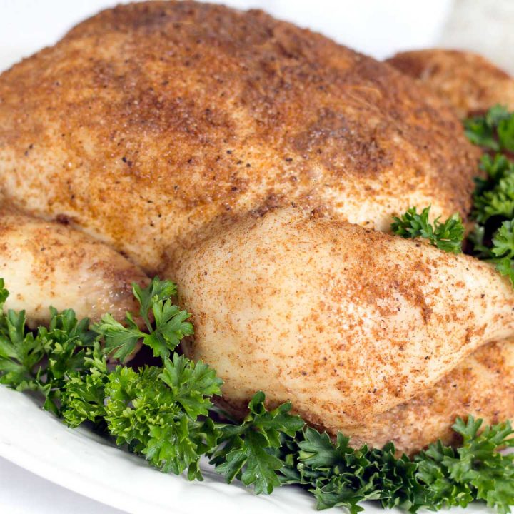 Whole cooked chicken covered with spices, on a white plate garnished with a lot of parsley.