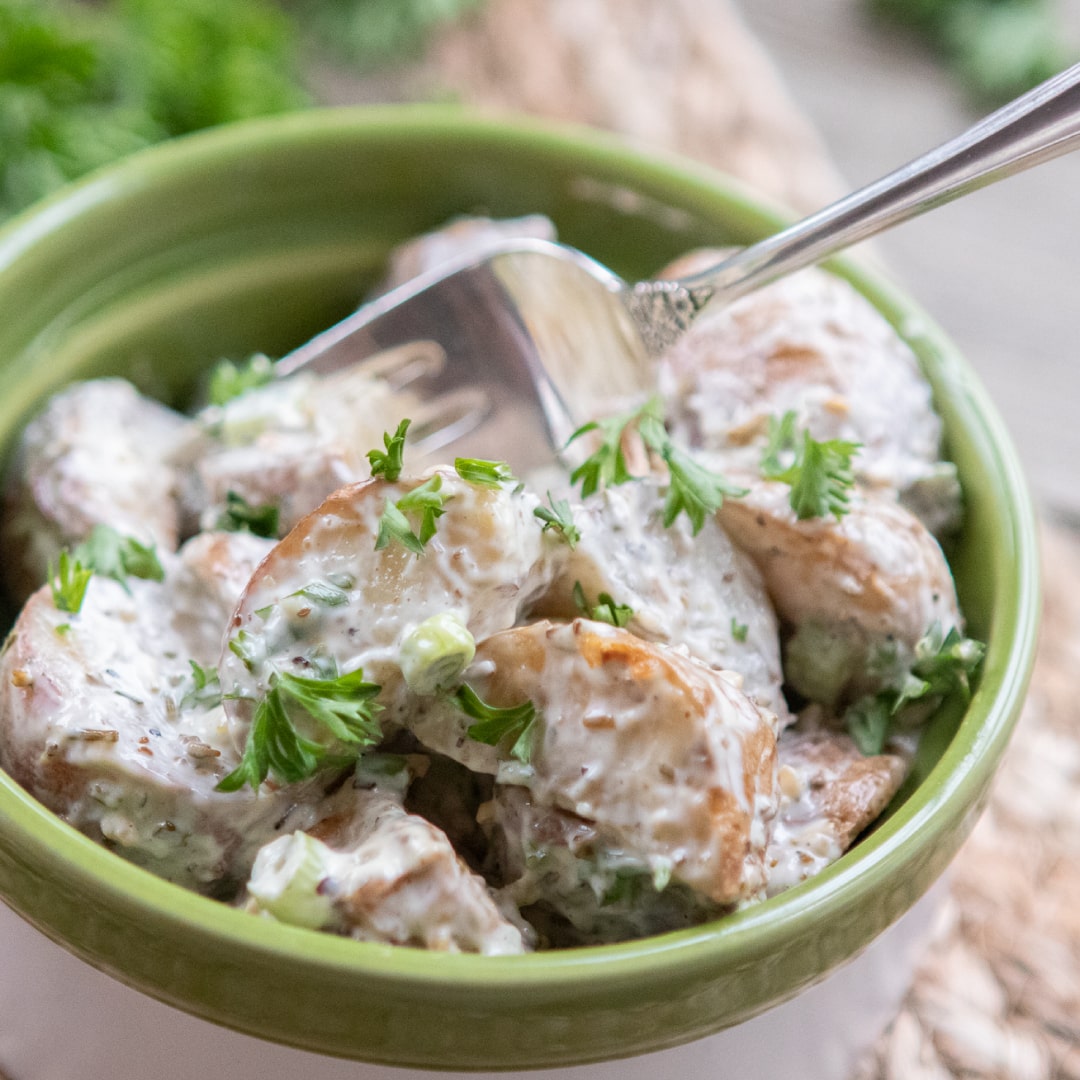 Bowl of potato salad garnished with parsley with a fork