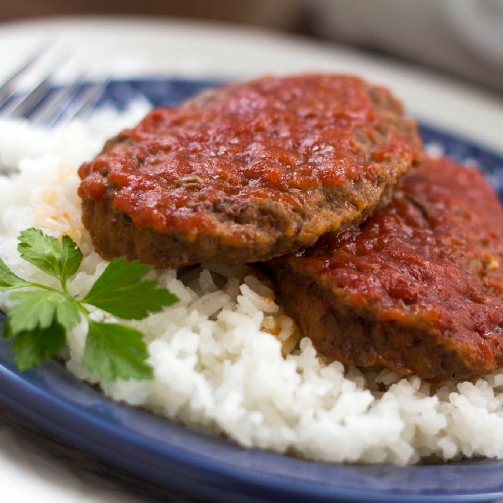 Two Baked Swiss Hamburgers on a bed of rice on a plate.