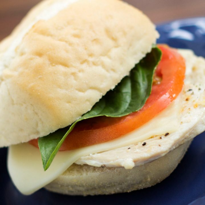 Turkey slice with mozzarella cheese, tomato, and basil on a white sandwich roll