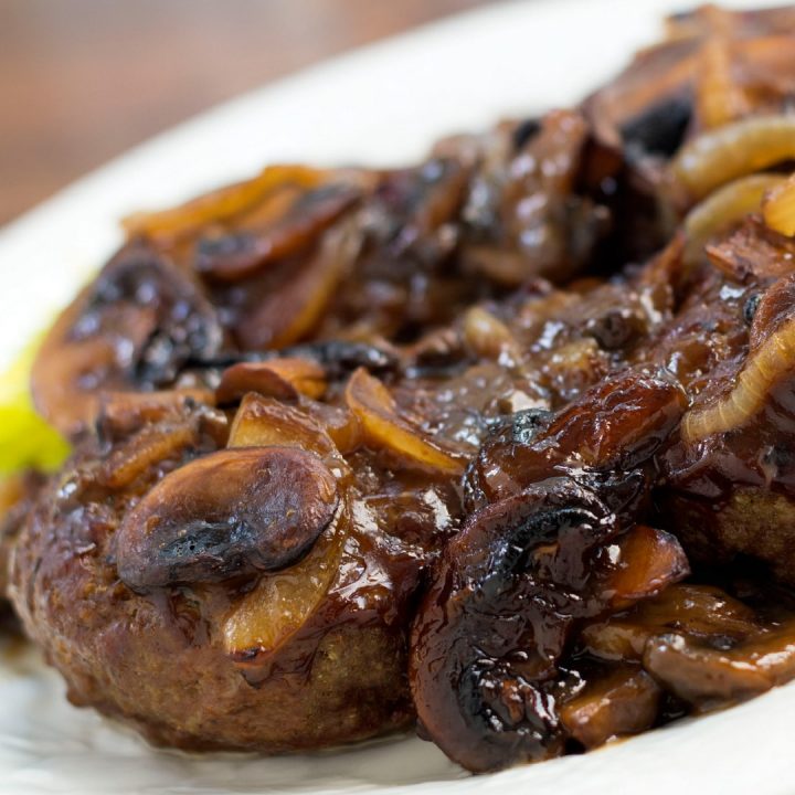 Hamburger patty covered with sliced mushrooms and onions and gravy on a white plate