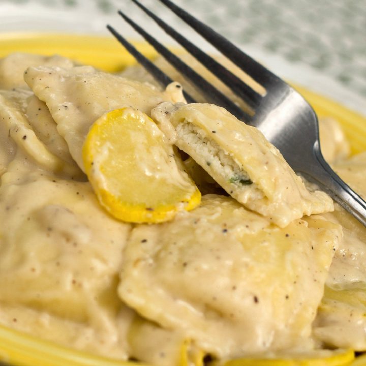 A yellow plate with cheese ravioli and slices of yellow squash covered with cheese sauce. There is a fork on top of the ravioli.