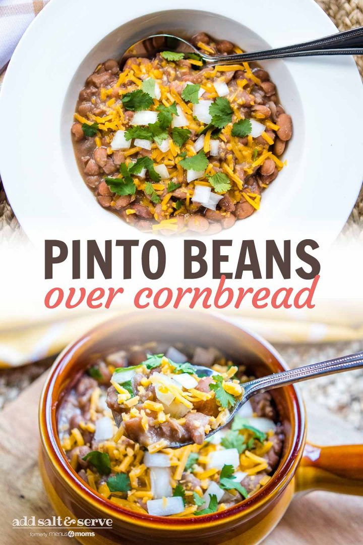 A spoonful of cooked pinto beans topped with shredded cheddar cheese and cilantro. Below the spoon is a bowl with a handle on a wooden cutting board and there is a yellow and white napkin on the edge of the cutting board. The bowl is full of cooked pinto beans topped with diced onions, shredded cheddar cheese, and cilantro.