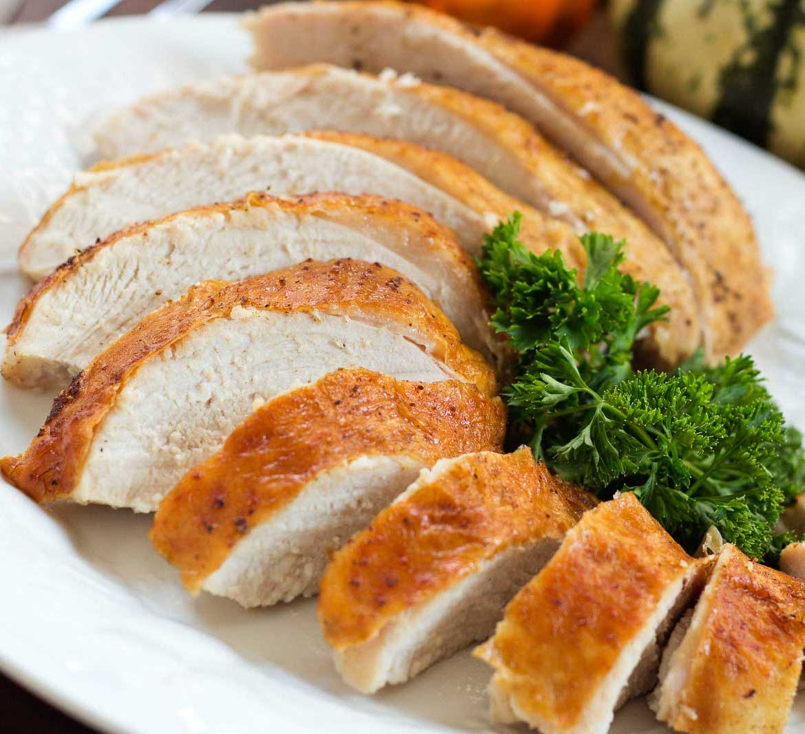 Sliced roasted turkey breast with golden brown skin on a white plate garnished with parsley