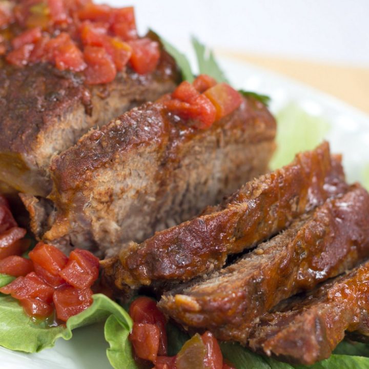 Sliced pot roast on a white plate and a bed of lettuce, garnished with diced tomatoes.