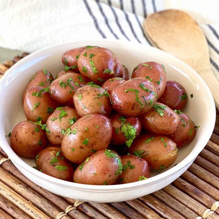 Bowl of boiled red potatoes coated in butter and garnished with chopped parsley