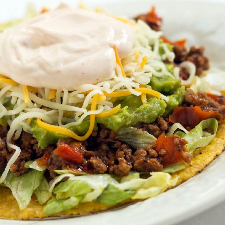 A plate with beef tostados made with guacamole, shredded cheese, and sour cream.