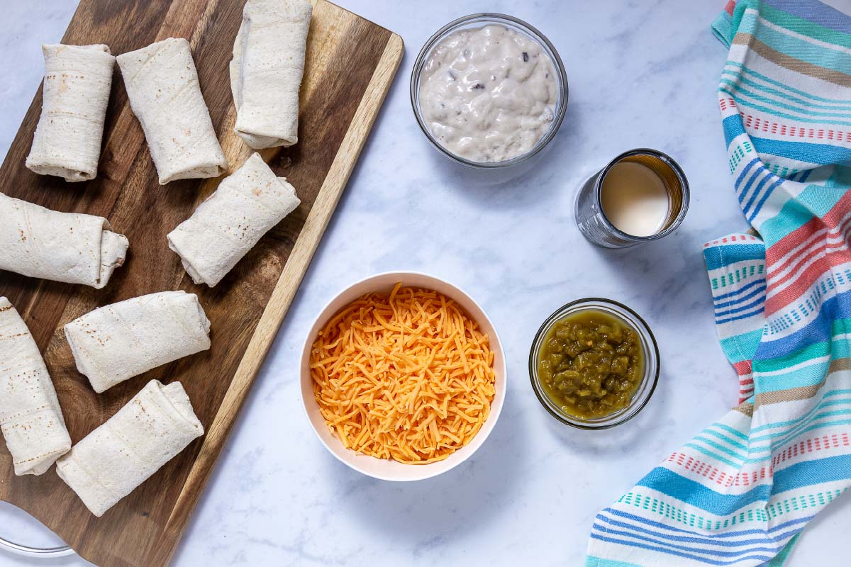 Ingredients for frozen burrito casserole: frozen burritos, condensed cream of mushroom soup, milk, green chilies, and shredded cheddar cheese.