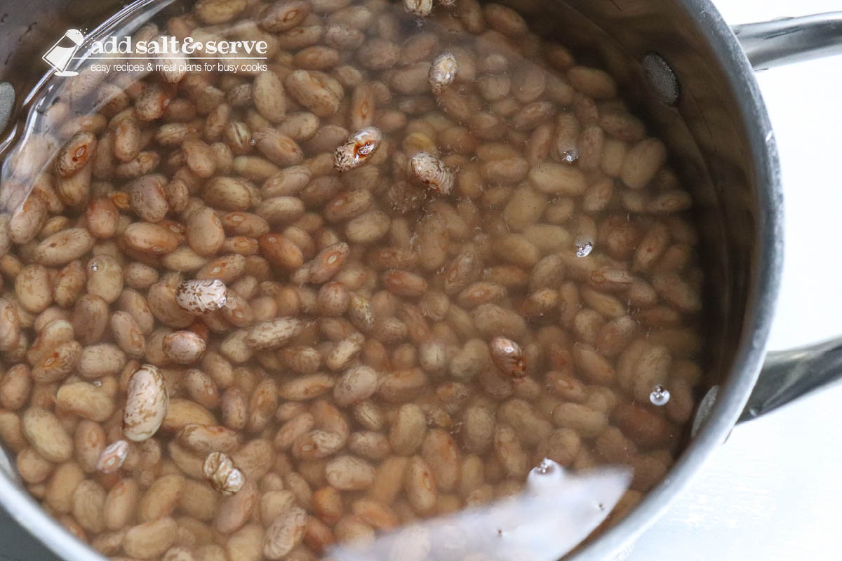 Uncooked pinto beans in a large pot covered in water.