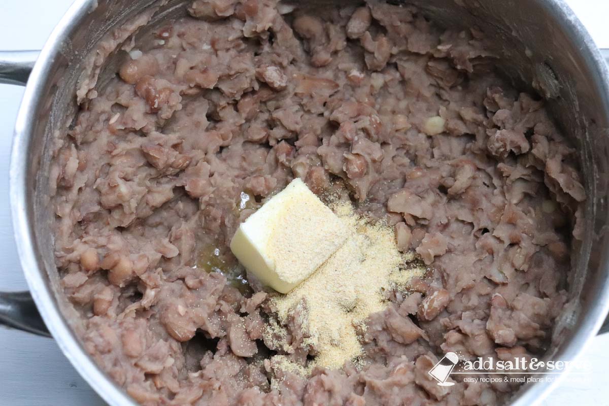 Cooked pinto beans in a large pot with a chunk of butter and adobo seasoning before mixing in.