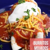 Burrito mojado topped with shredded cheddar, sour cream, and chopped cilantro.
