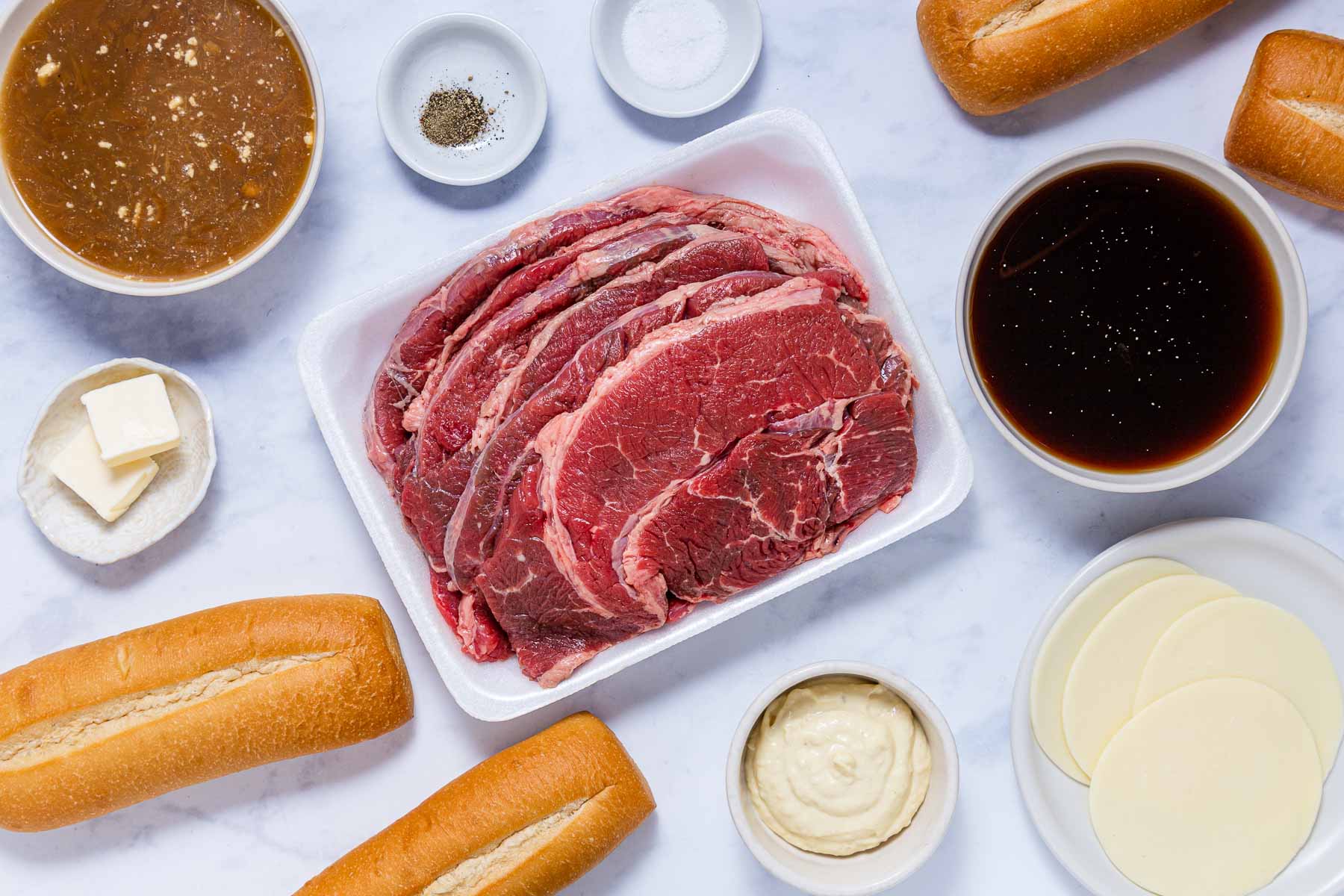 Ingredients for Fench Dip Sandwiches: French onion soup, beef consommé, hoagie rolls, salt, pepper, mayonnaise, provolone cheese, butter, and sliced chuck roast.