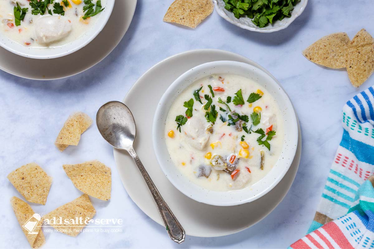 Two bowls of Southwest Chicken Corn Chowder on saucers with cilantro and tortilla chips to the side.