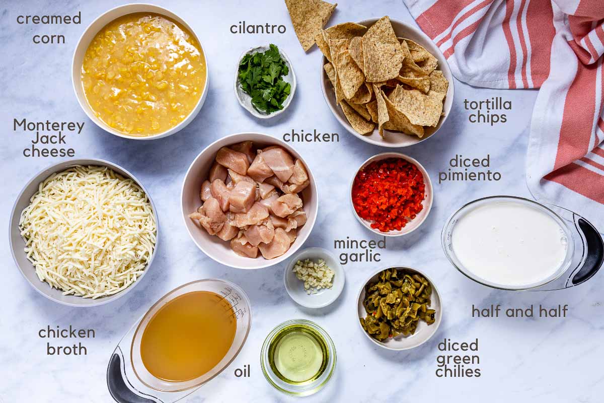 Ingredients for Southwest Chicken Corn Chowder: chopped chicken, shredded Monterey Jack cheese, creamed corn, minced garlic, chicken broth, green chilies, diced pimento, vegetable oil, half and half, cilantro, and tortilla chips.