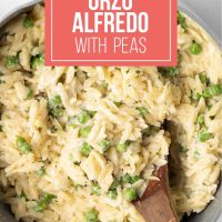 Serving of Orzo Alfredo with peas on a wooden spoon in a pot.