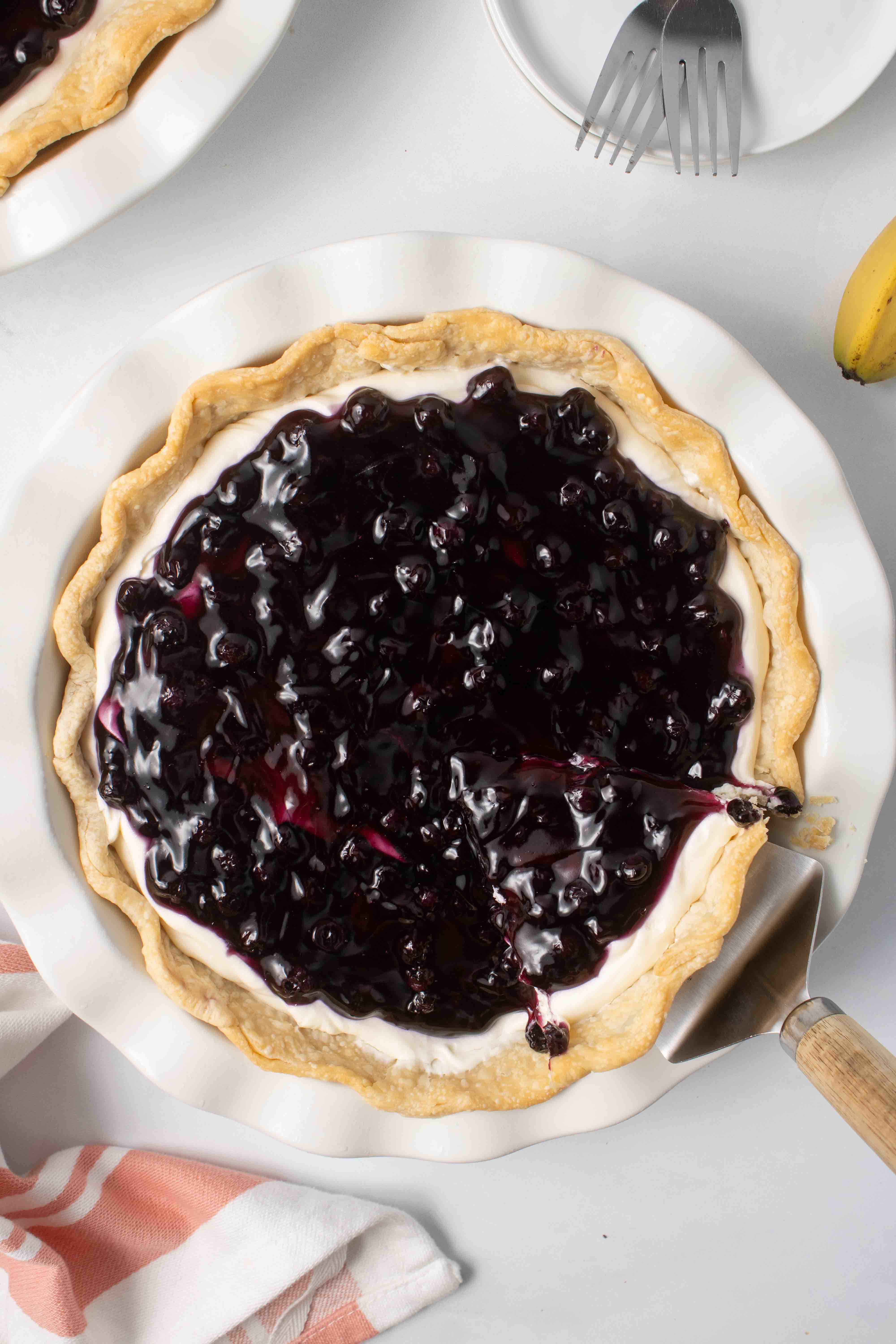 Overhead view of a blueberry banana pie with a slice being lifted out.