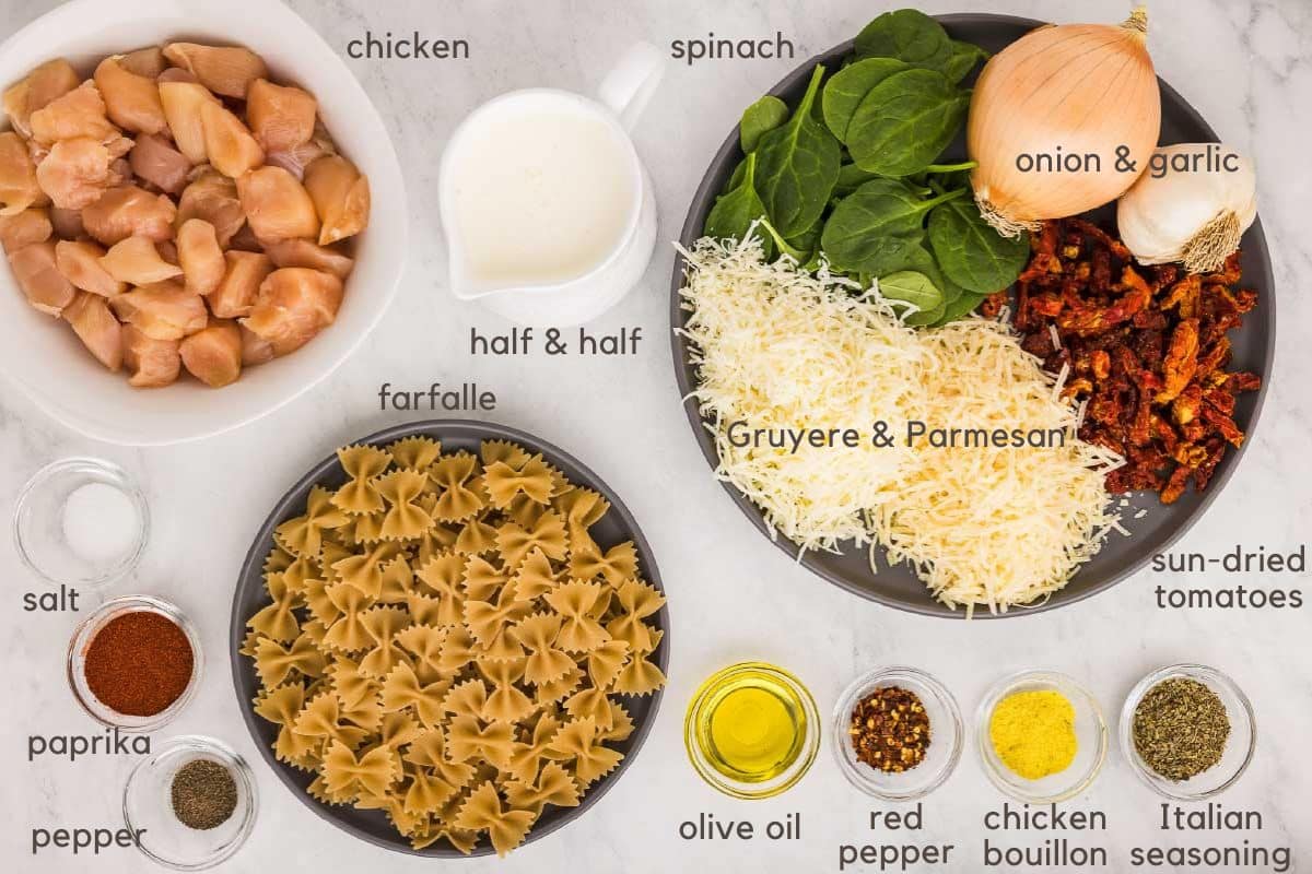 Ingredients for Creamy Tuscan Chicken: cubed chicken breasts, cream, spinach, yellow onion, garlic, shredded gruyere, shredded Parmesan, sun-dried tomatoes, Italian seasoning, chicken bouillon, red pepper flakes, olive oil, mini farfalle, paprika, pepper, and salt.