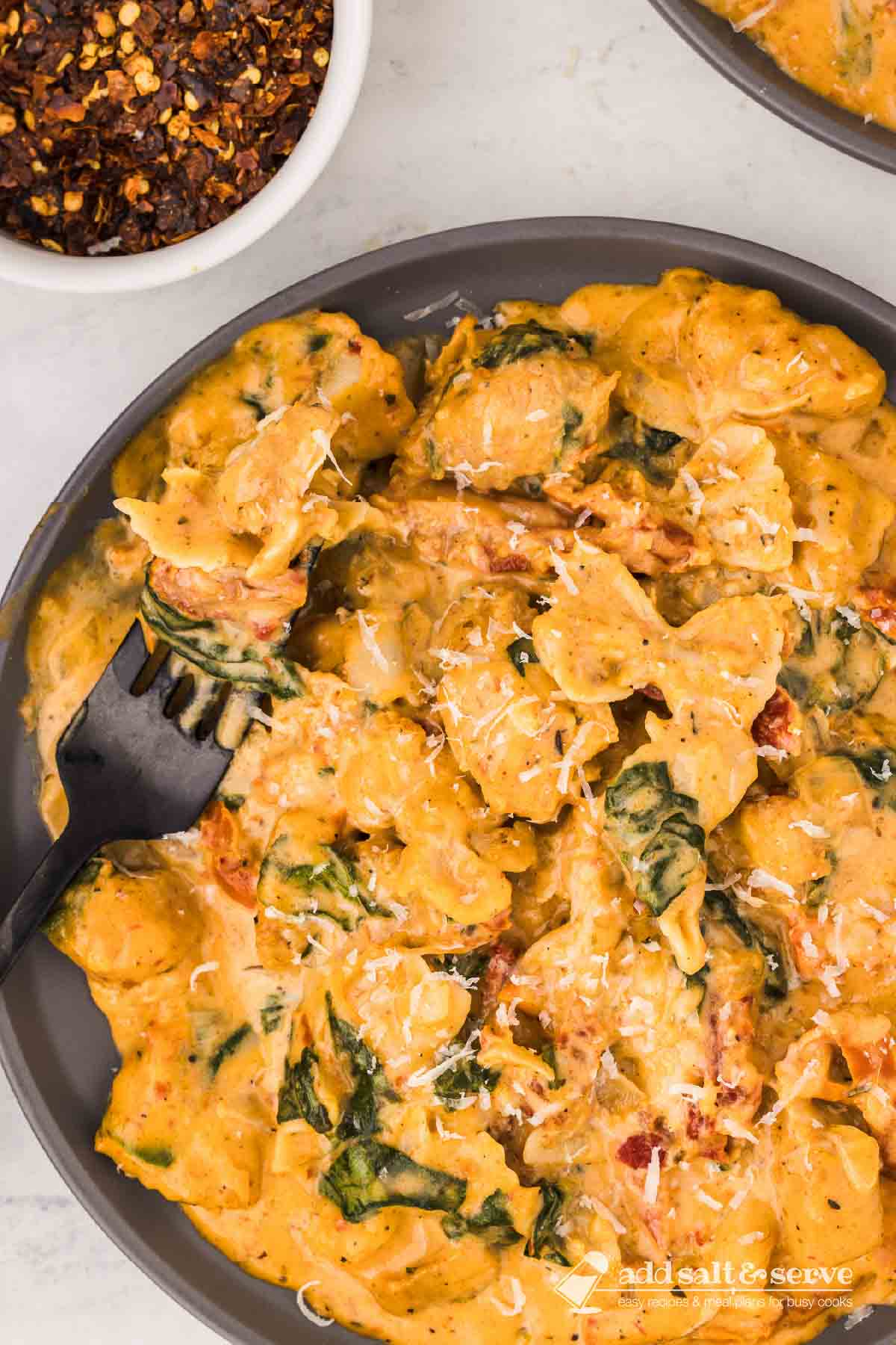 Creamy Tuscan chicken with sun-dried tomatoes, spinach, and mini farfalle in cream sauce on a plate with a forkful on a fork resting on the plate.