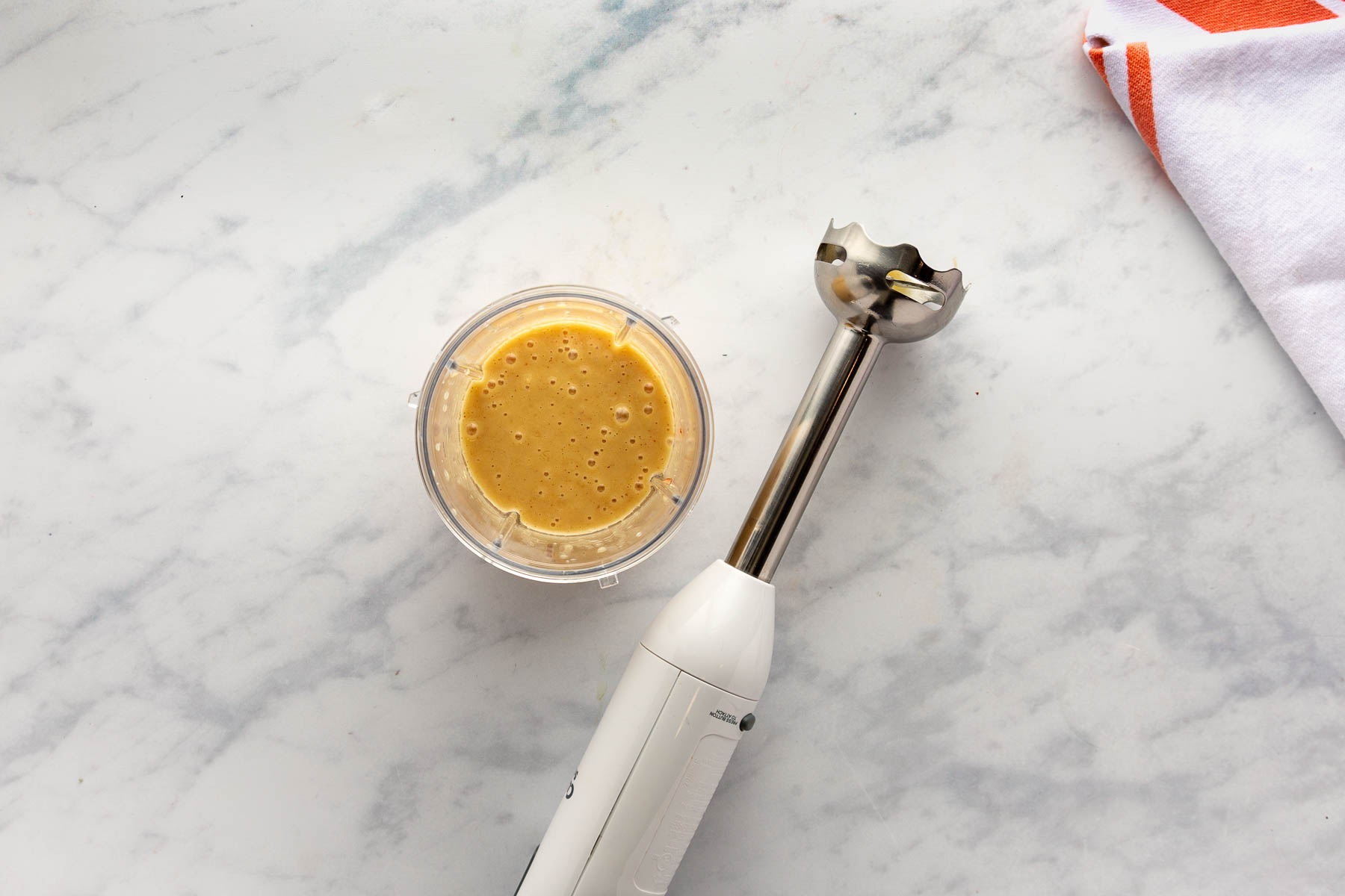 Ingredients for Sesame Ginger Dressing in a container beside an immersion blender after blending.