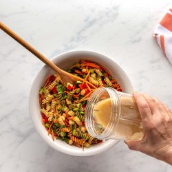 Pouring sesame ginger dressing over Thai pasta Salad.