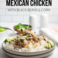 A plate of shredded chicken in a creamy sauce with black beans, corn, tomatoes, and green chilies served over rice and garnished with sliced avocado, shredded cheese, fresh cilantro, and lime wedges beside a bowl of fresh cilantro and a bowl with lime with text Slow Cooker Mexican Chicken with Black Beans & Corn.