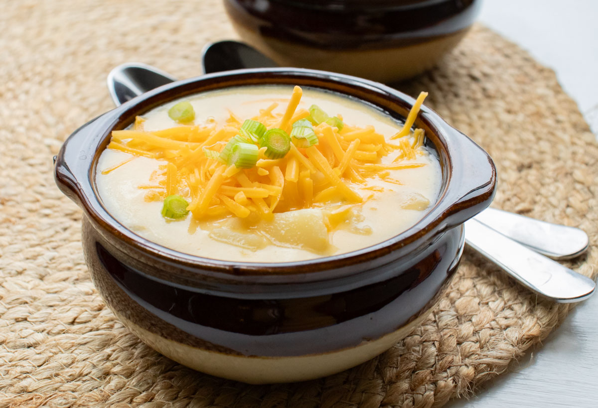 Potato soup with hash browns in a bowl and garnished with shredded cheddar cheese and sliced green onions.