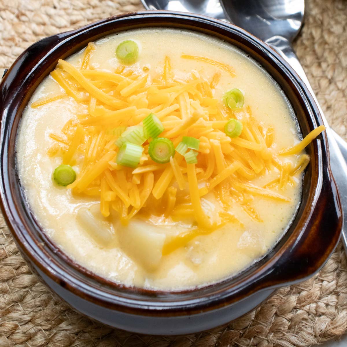 Potato soup with hash browns in a bowl and garnished with shredded cheddar cheese and sliced green onions.