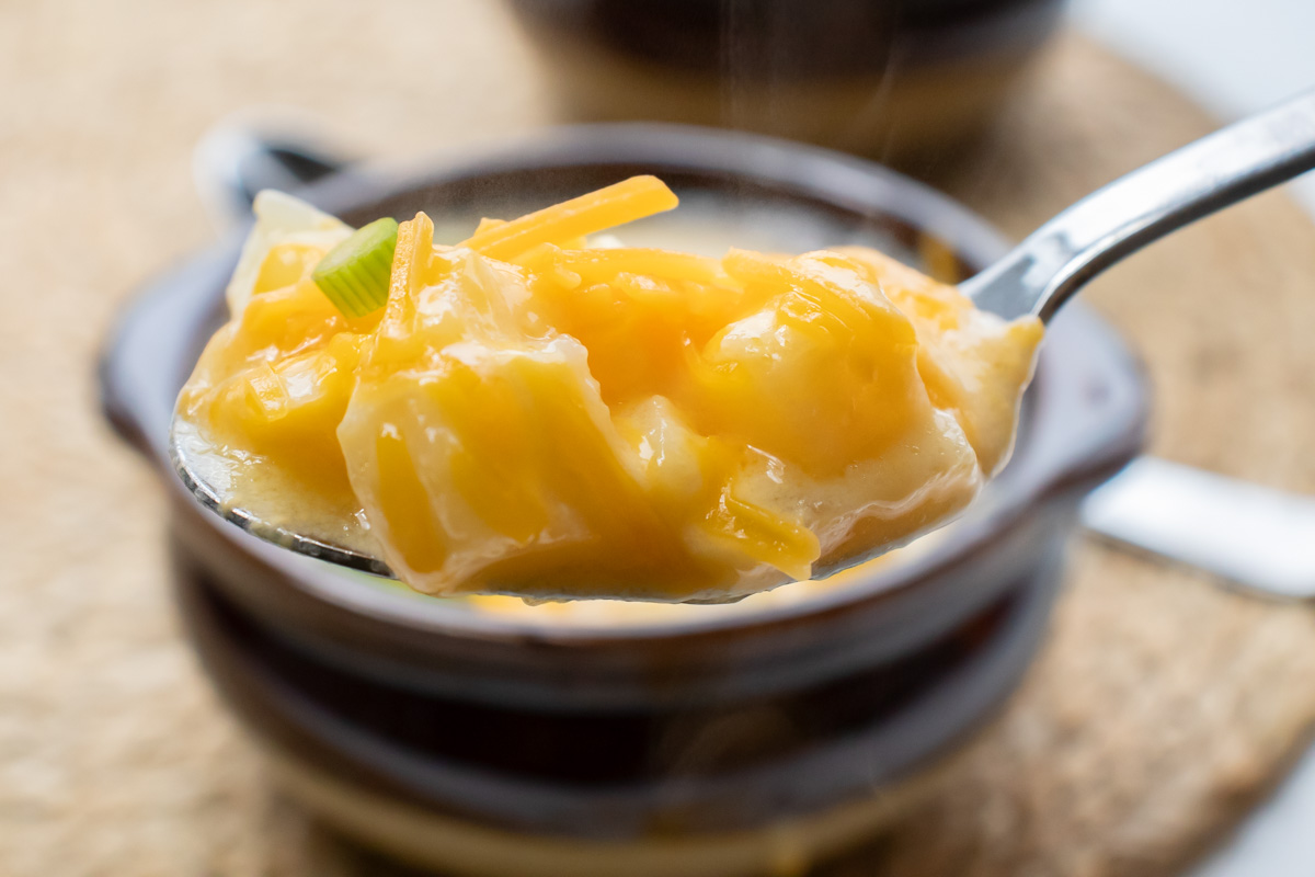 Spoonful of potato soup with hash browns held in front of a bowl of the soup.