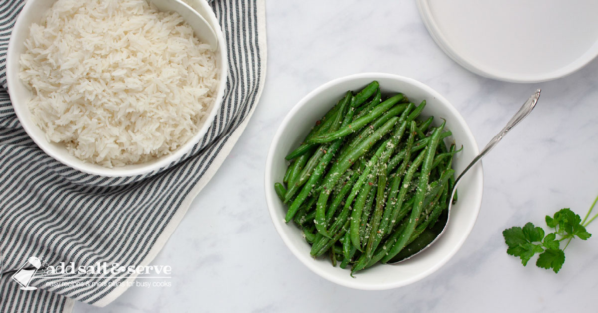 A serving bowl of cooked Seasoned Green Beans beside a serving bowl of white rice.