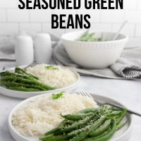 Seasoned green beans garnished with Parmesan cheese on plates with white rice with a serving bowl of green beans in the background and text Italian Seasoned Green Beans.