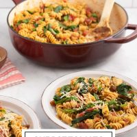 Two plates of Tomato Spinach Pasta garnished with Parmesan cheese and fresh basil strips on a counter beside the pan of the full dish and a small bowl of fresh basil strips with text One Pot Tomato Spinach Pasta.