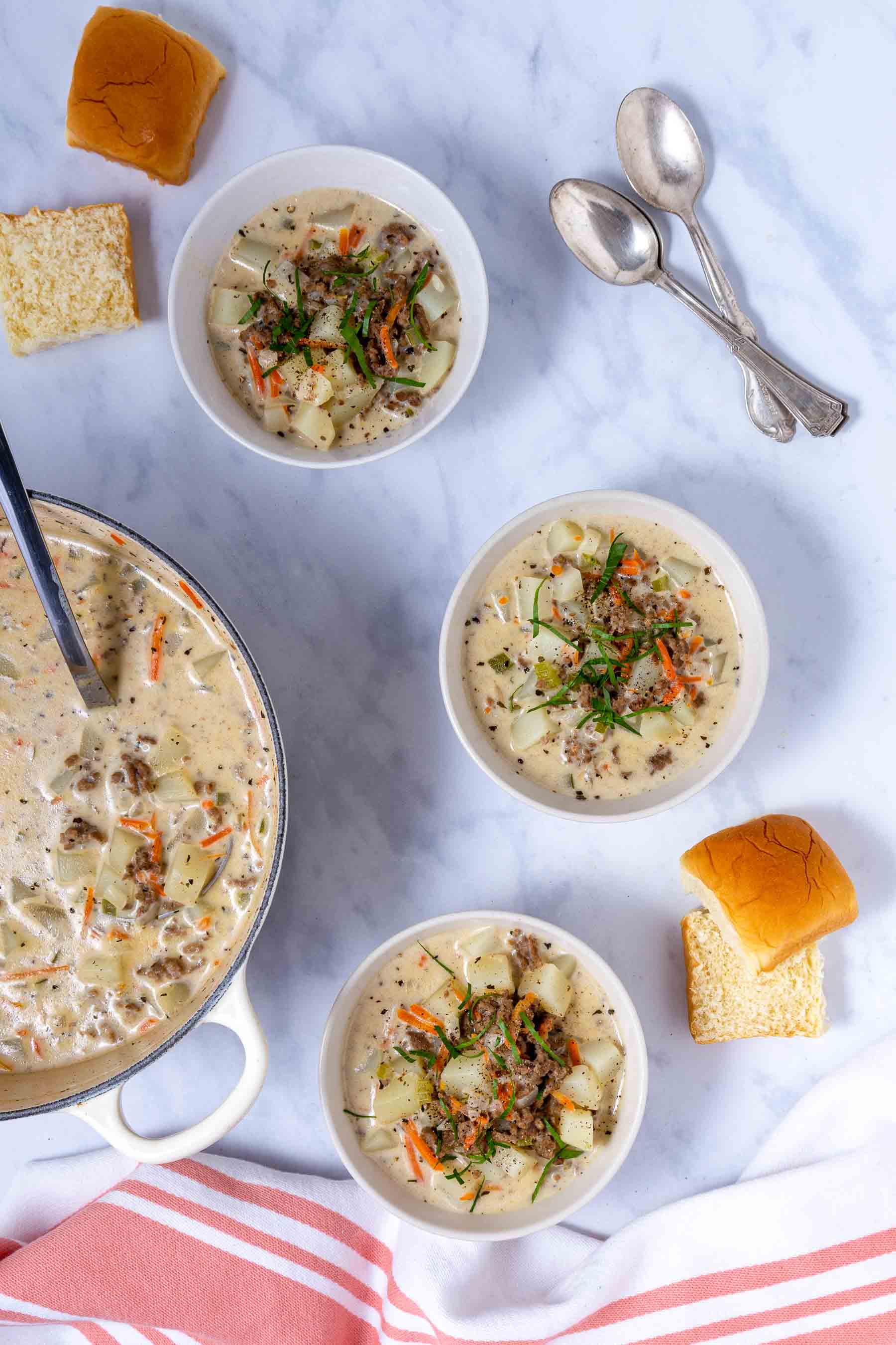 Three bowls of Cheeseburger Soup with Velveeta on a counter beside a soup pot full of the soup..