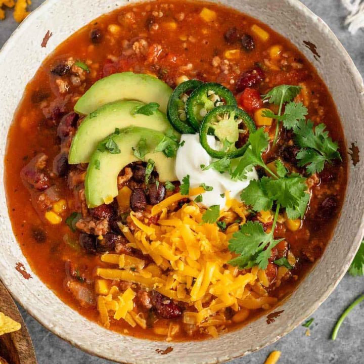 Bowl of taco soup garnished with shredded cheddar cheese, sour cream, jalapeño, cilantro, and avocado.