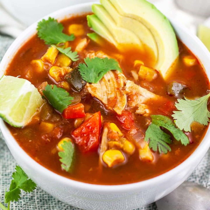 Bowl of slow cooker chicken corn soup garnished with cilantro, lime, and avocado.