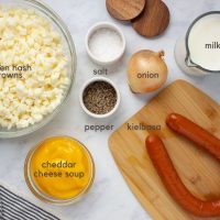 Ingredients for cheesy potato kielbasa soup crockpot: frozen hash browns, condensed cheddar cheese soup, kielbasa, onion, milk, salt and pepper.