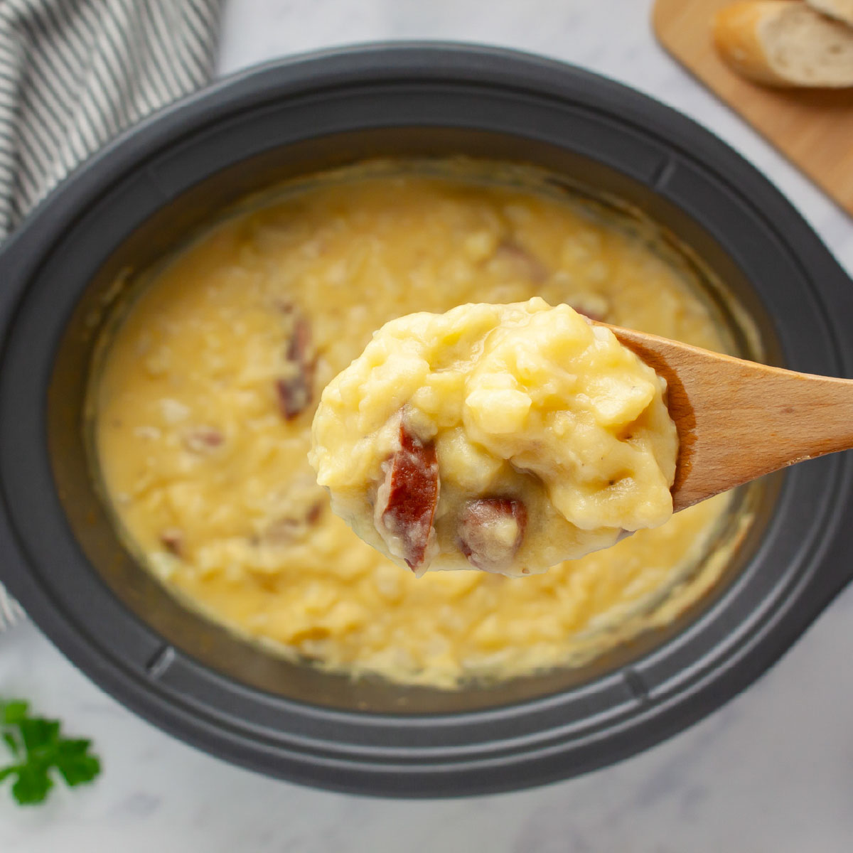 Close-up of a spoonful of potato soup with kielbasa pieces on a wooden spoon held over a crockpot of the soup.