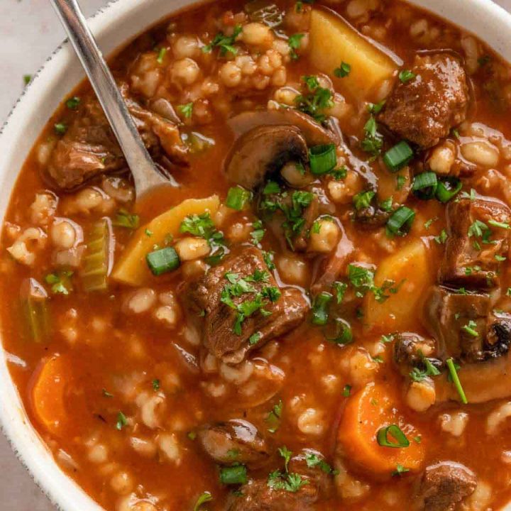 Bowl of crockpot beef and barley soup garnished with parsley and green onion.