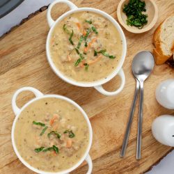 Two bowls of hash brown soup in white crocks beside fresh basil strips in a small bowl and two spoons.