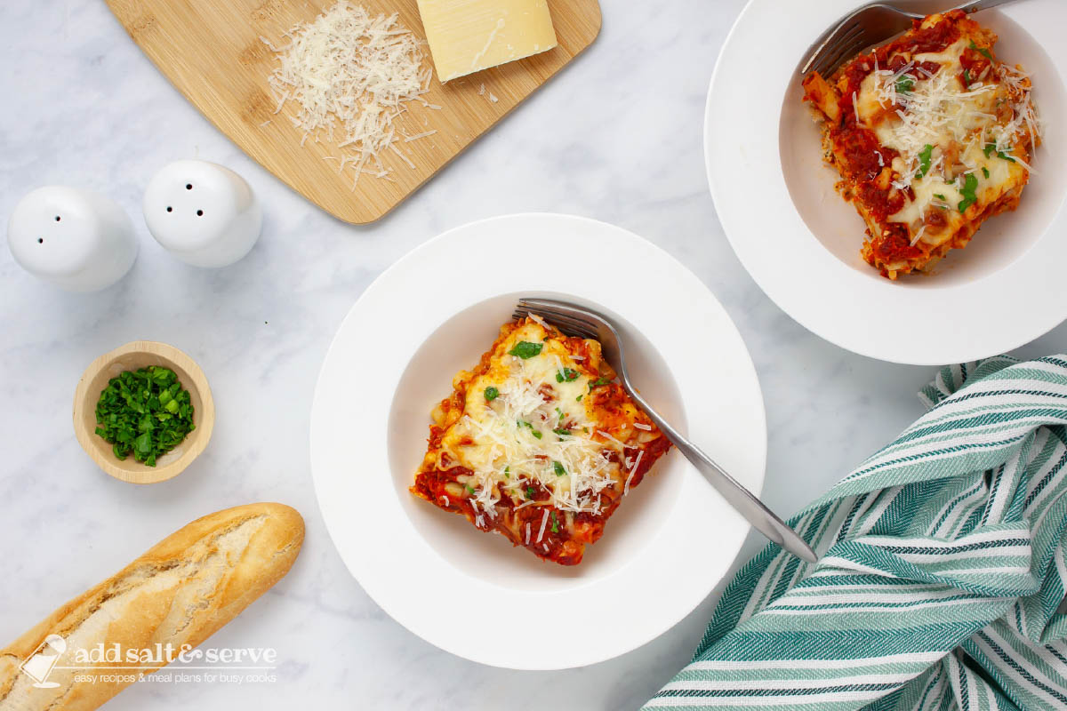 Bowl of cheesy meatless baked ziti garnished with fresh parsley and grated Parmesan cheese.