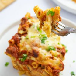 Forkful of Cheesy Meatless Baked Ziti garnished with fresh parsley held above a serving of the ziti on a plate.